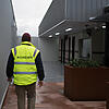 Image of a person in a high resolution vest with the word "Biosecurity" written on it, walking away from the camera towards a building entrance
