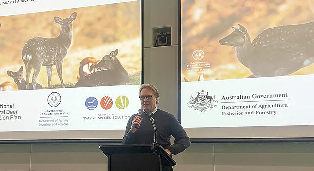Image of a person standing in front of a presentation screen - they are Dr Bertie Hennecke speaking at the launch of the National Feral Deer Action Plan