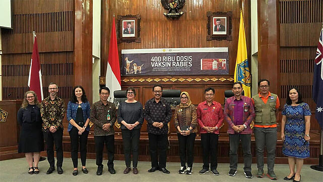 Image of 11 people standing in front of a banner and some flags at the Rabies vaccine handover event in Bali