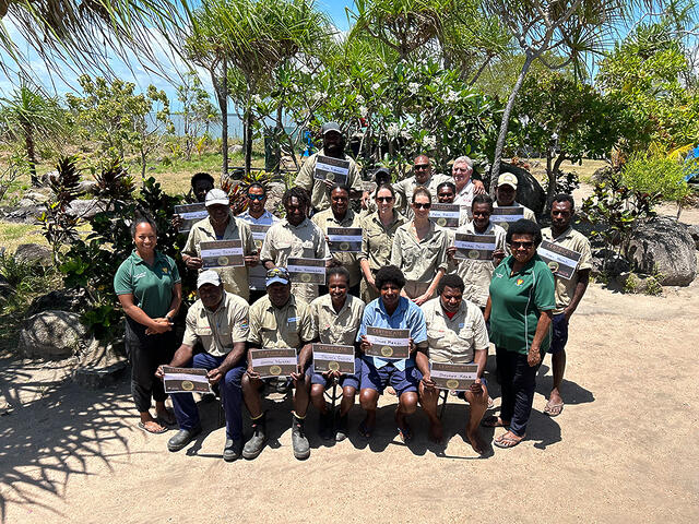 Image of a large croup of people sitting outside, holding up certificates; they are rangers who have completed refresher fruit fly trapping training program, alongside trainers from DAFF and NAQIA.