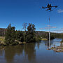 Image of a drone flying over a river surrounded by greenery, collecting a water sample
