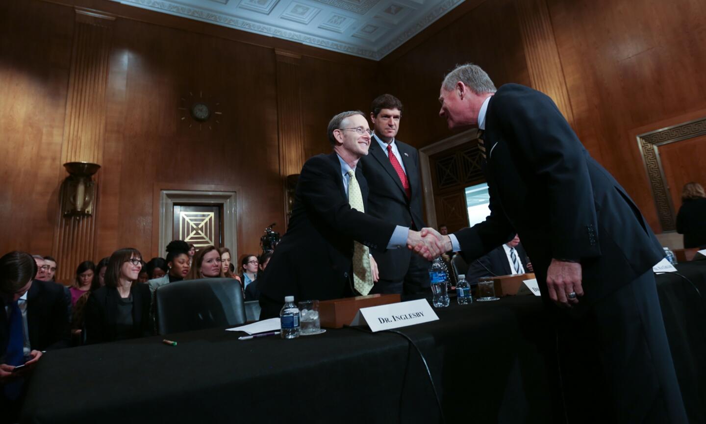 Two men shake hands in a room with dark wood walls