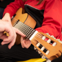 Close up of a child holding a guitar as an adult points to where he should put his fingers