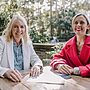 Two women sit at a cafe in an outdoor area. They are both smiling. There are pamphlets on the table in front of them. Photo: Michael Gray