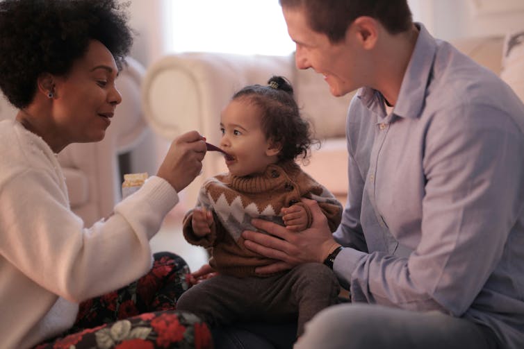 A mother and father feed a small child peanut butter.