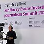 A video camera operator, with camera, stood in front of a large sign for the Truth Tellers summit