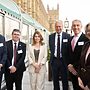 Four men and two women standing outside Houses of Parliament looking at camera