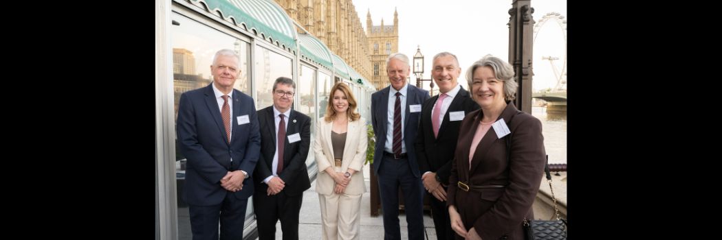 Four men and two women standing outside Houses of Parliament looking at camera