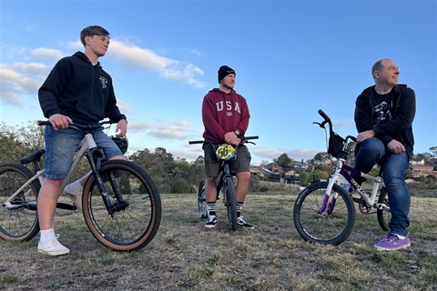 Three men sit on their BMX bikes in an open field