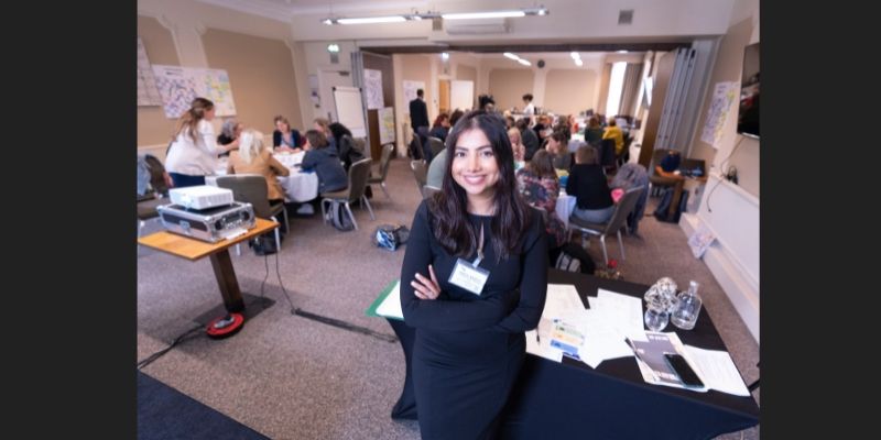 Researcher stands at the front of a busy room
