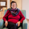 Woman in a red jumper and colourful scarf sitting on a chair