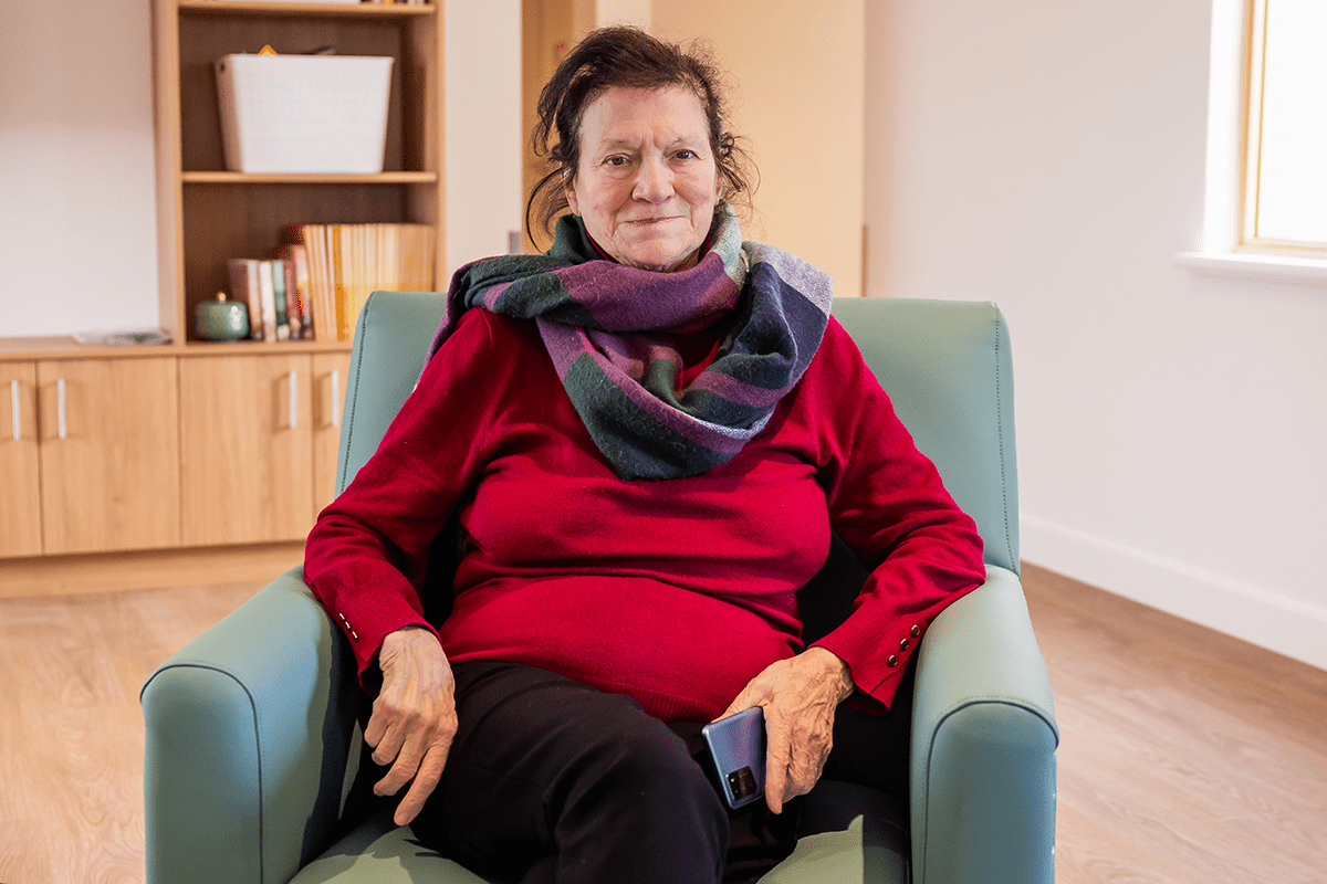 Woman in a red jumper and colourful scarf sitting on a chair