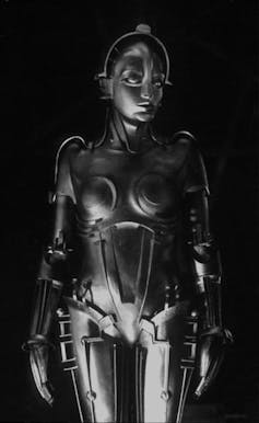 Black and white historical photo of a metallic female shaped robot with various decorative elements.
